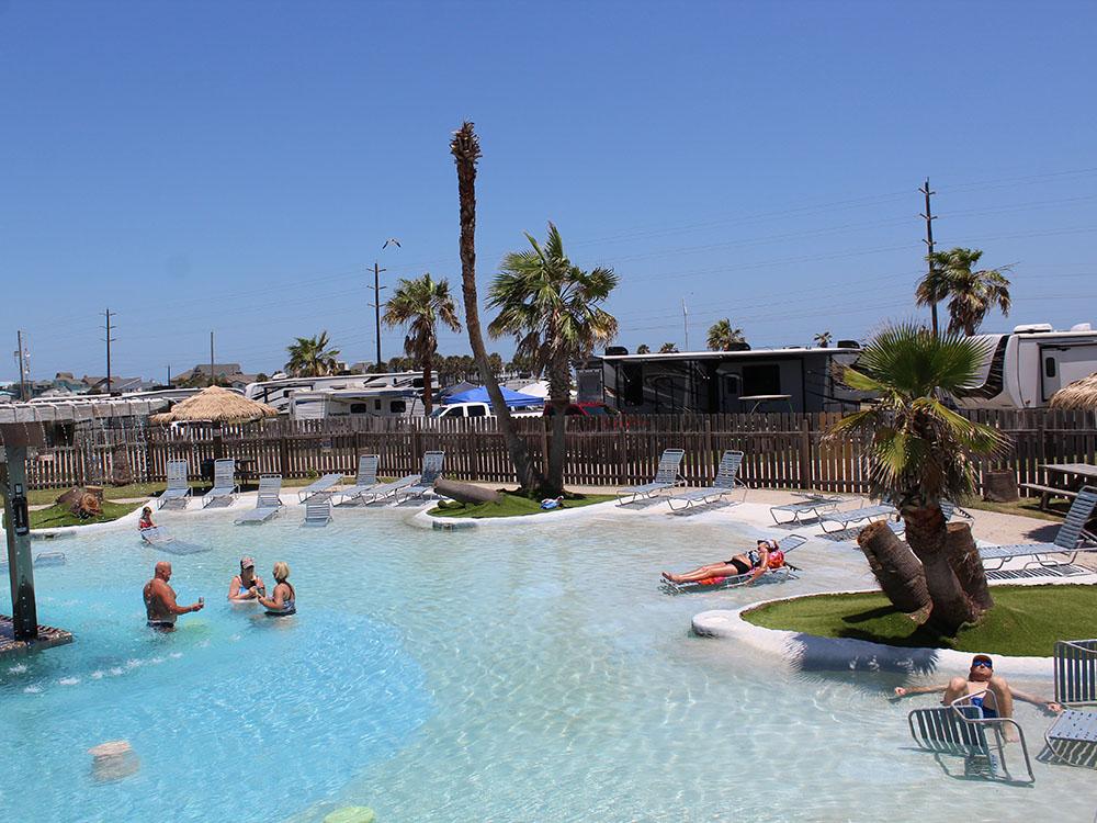 Guests enjoying the pool area surrounded by palm trees at Jamaica Beach RV Resort in Galveston, Texas